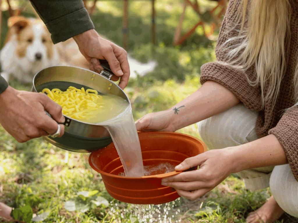 Man pouring pasta water into orange strainer held by a woman with an arm tattoo