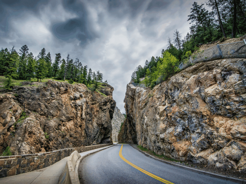 Road going through a canyon of rocks with trees on top. Things to do in Kootenay National Park - Sinclair Canyon