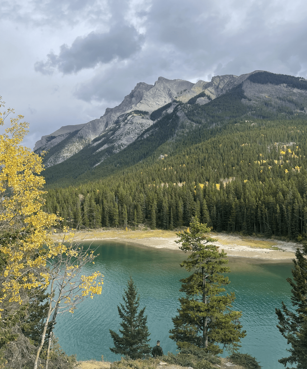Lake Minnewanka in Banff National Park with turquoise water, evergreen forest, and Rocky Mountain peaks under a cloudy sky.